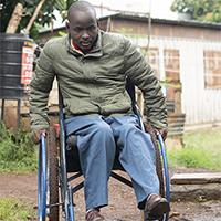 Edwin Opetu Oboyo using a wheelchair on rough terrain